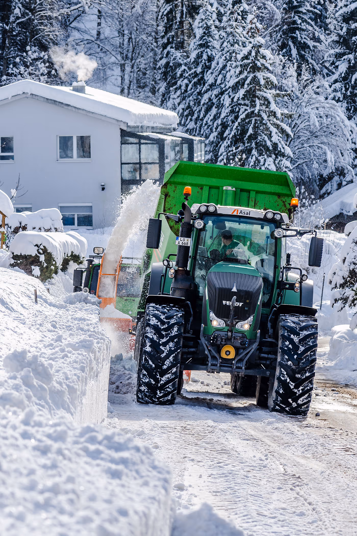 Schneefräse wirft Schnee in den Anhänger eines Traktors bei der Schneeräumung in einSchneefräse wirft Schnee in den Anhänger eines Traktors bei der Schneeräumung in einem Wohngebiet.em Wohngebiet.