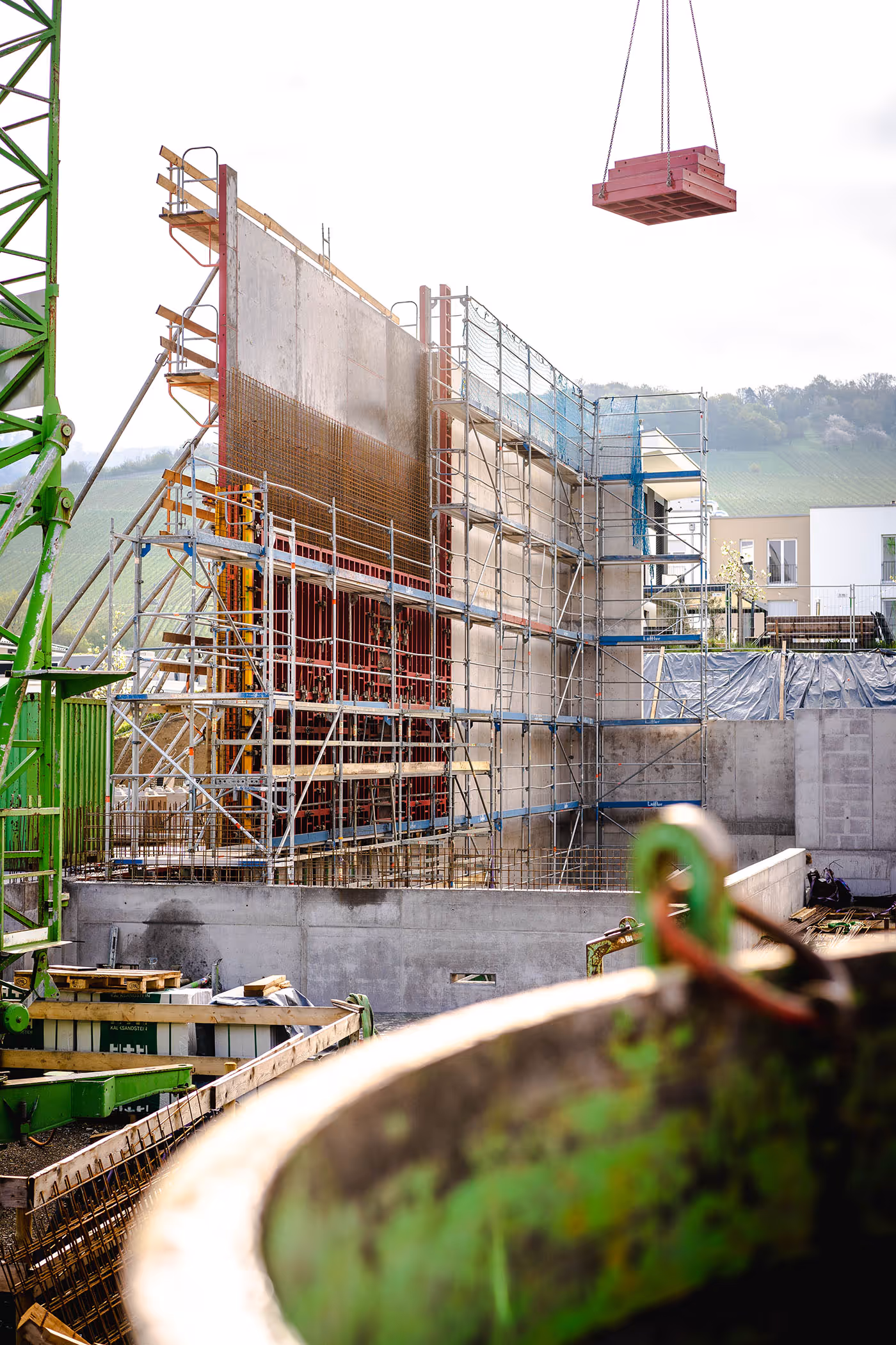 Baustelle mit Schalungselementen, Baugerüsten und einem schwebenden Materialpaket.