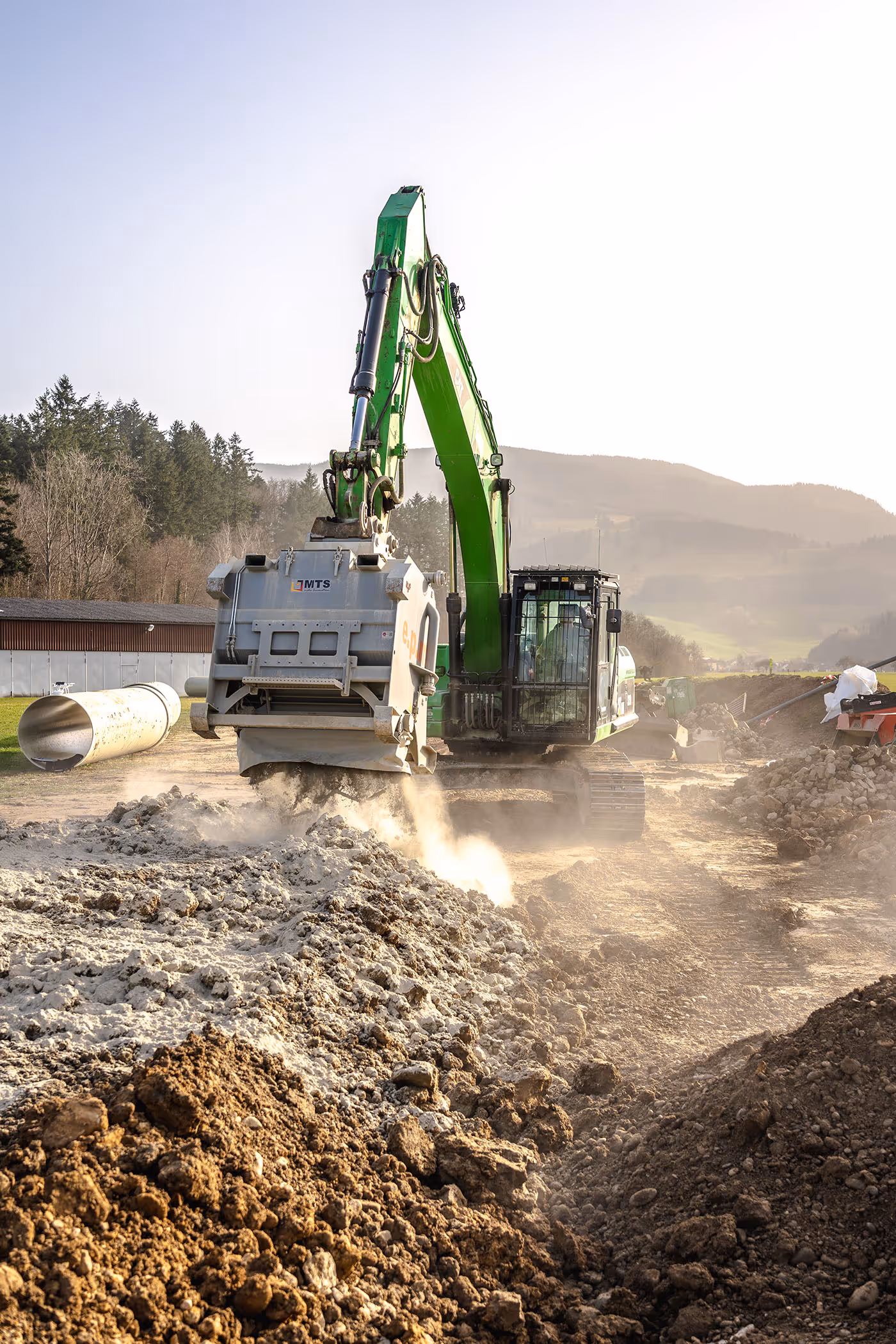 Asal-Bagger bei der Rohrbettung mit Brechmaterial auf einer Baustelle