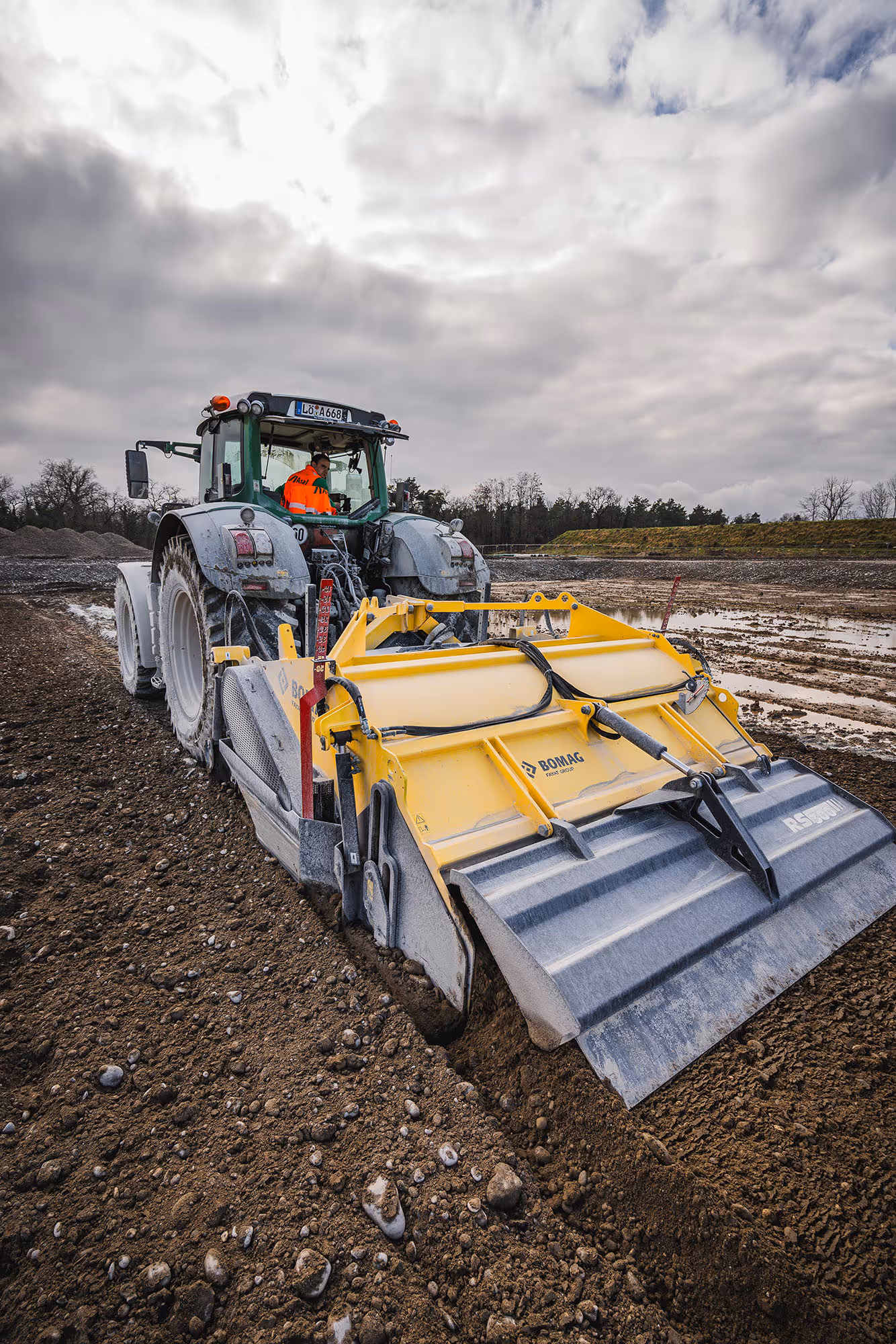 Traktor mit gelber Bodenfräse beim Stabilisieren von Bodenmaterial auf Baustelle.