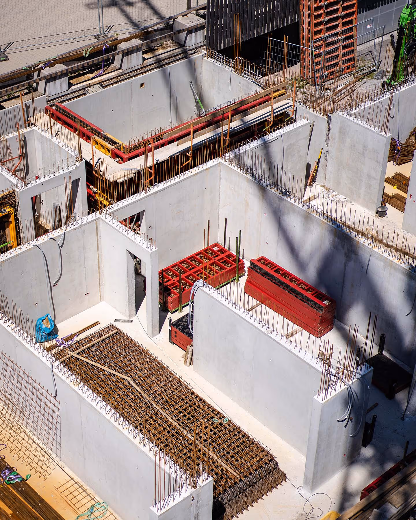 Baustelle mit bereits gemauerten Innenwänden eines Gebäudes, Stahlbewehrung sichtbar.