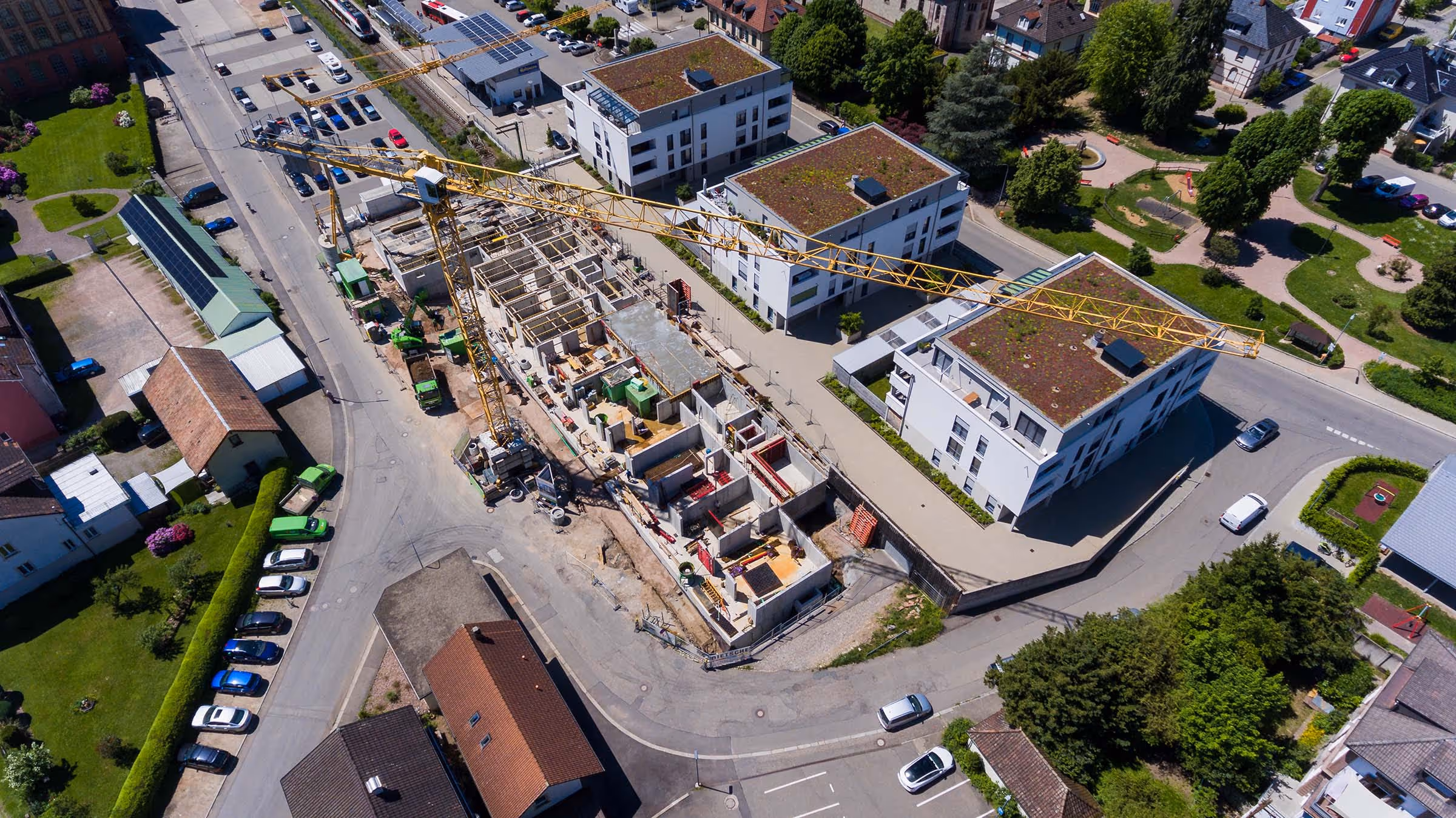 Großbaustelle eines Wohnprojekts in einer Wohnsiedlung mit mehreren Kränen, Rohbau und angrenzenden Mehrfamilienhäusern mit begrünten Dächern.