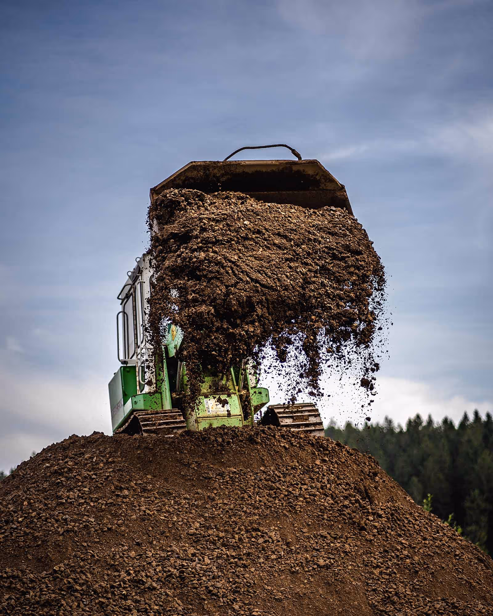 Raupenlader kippt lockeres Erd- oder Gesteinsmaterial von Erdwall