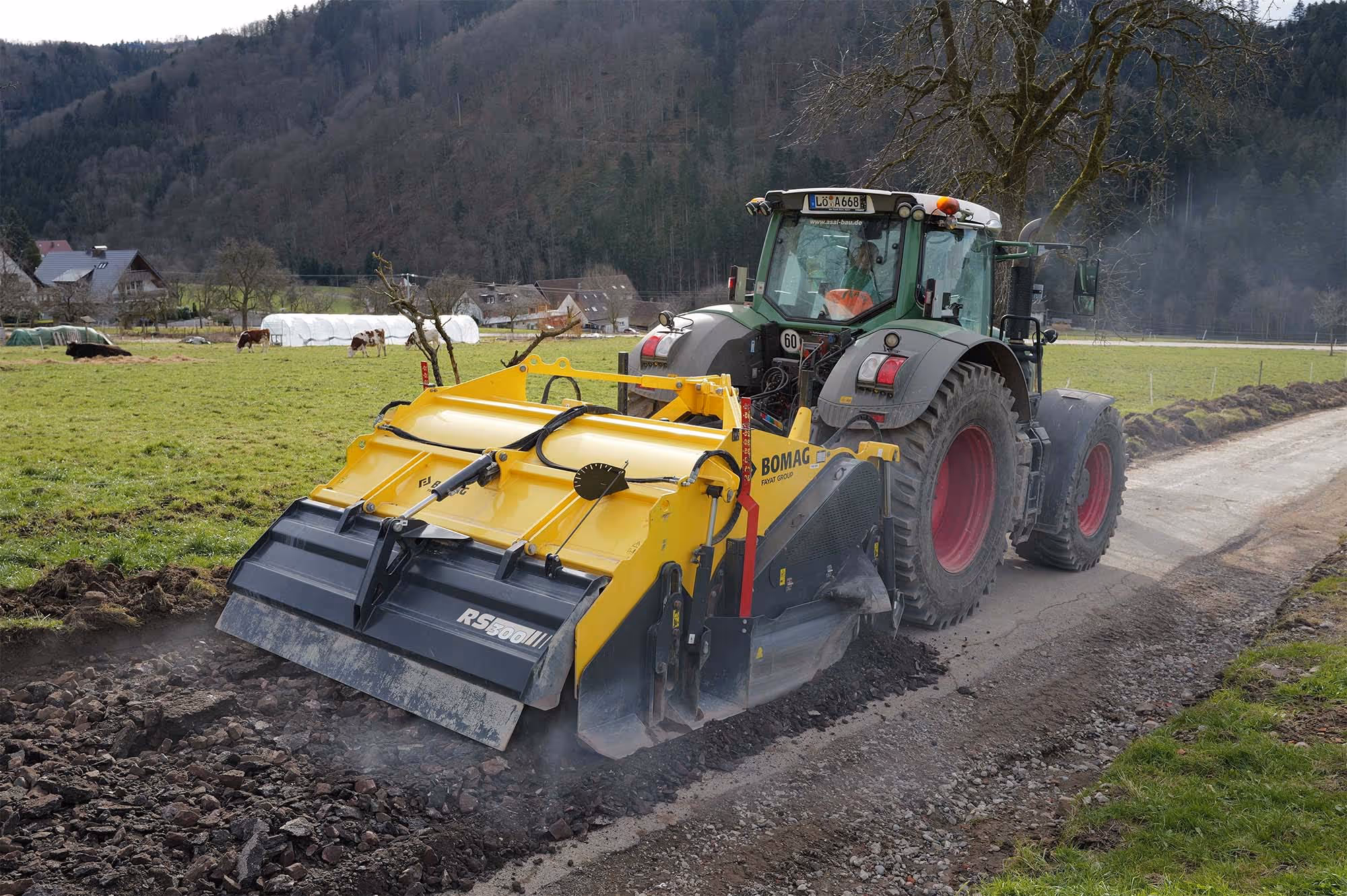 Traktor mit Bodenfräse beim Sanieren eines geschotterten Feldwegs im ländlichen Gebiet.