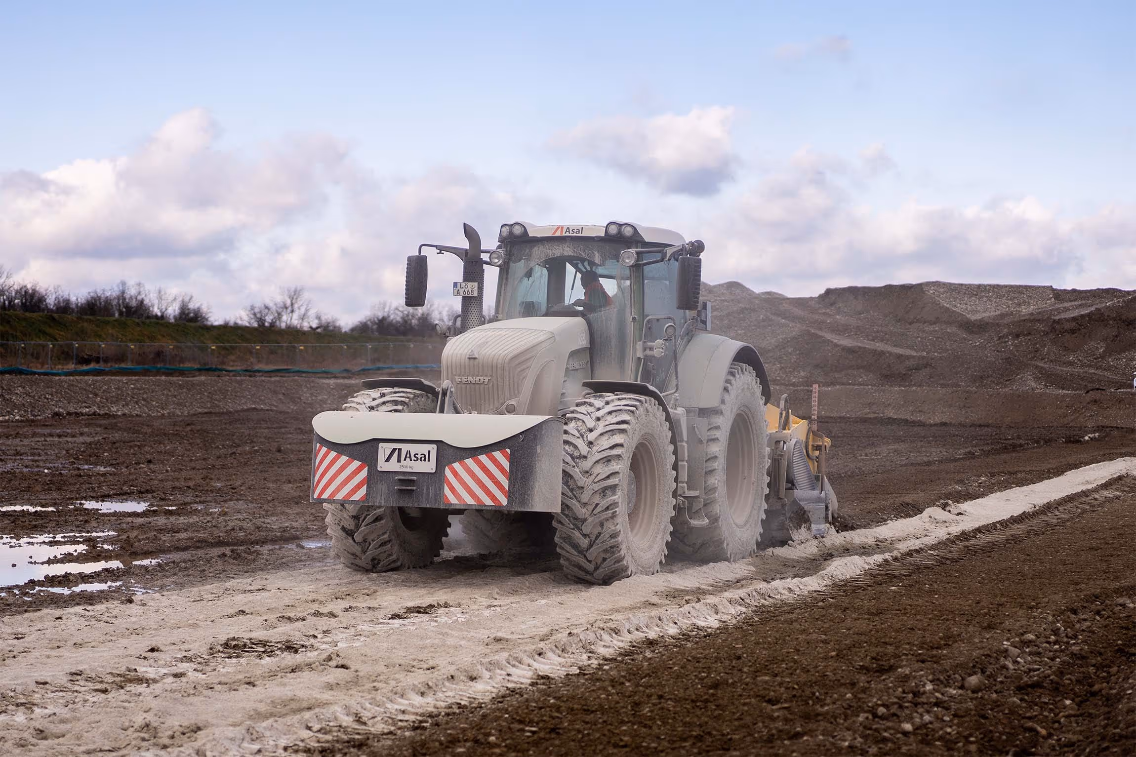 Traktor mit angebautem Bodenfräsgerät stabilisiert und mischt Kalk in den Boden ein.
