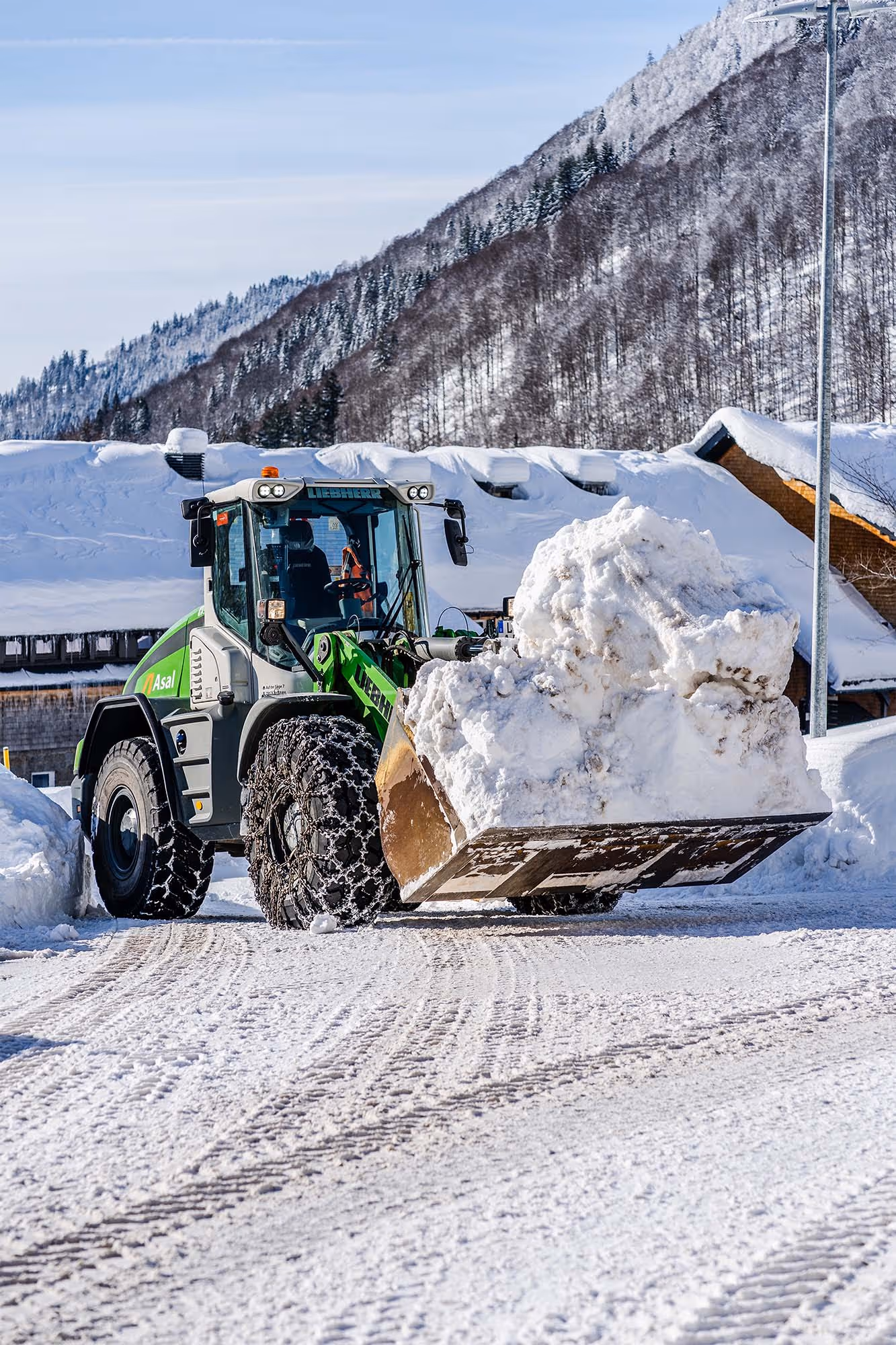 Radlader transportiert große Menge Schnee auf einem Parkplatz im Skigebiet.