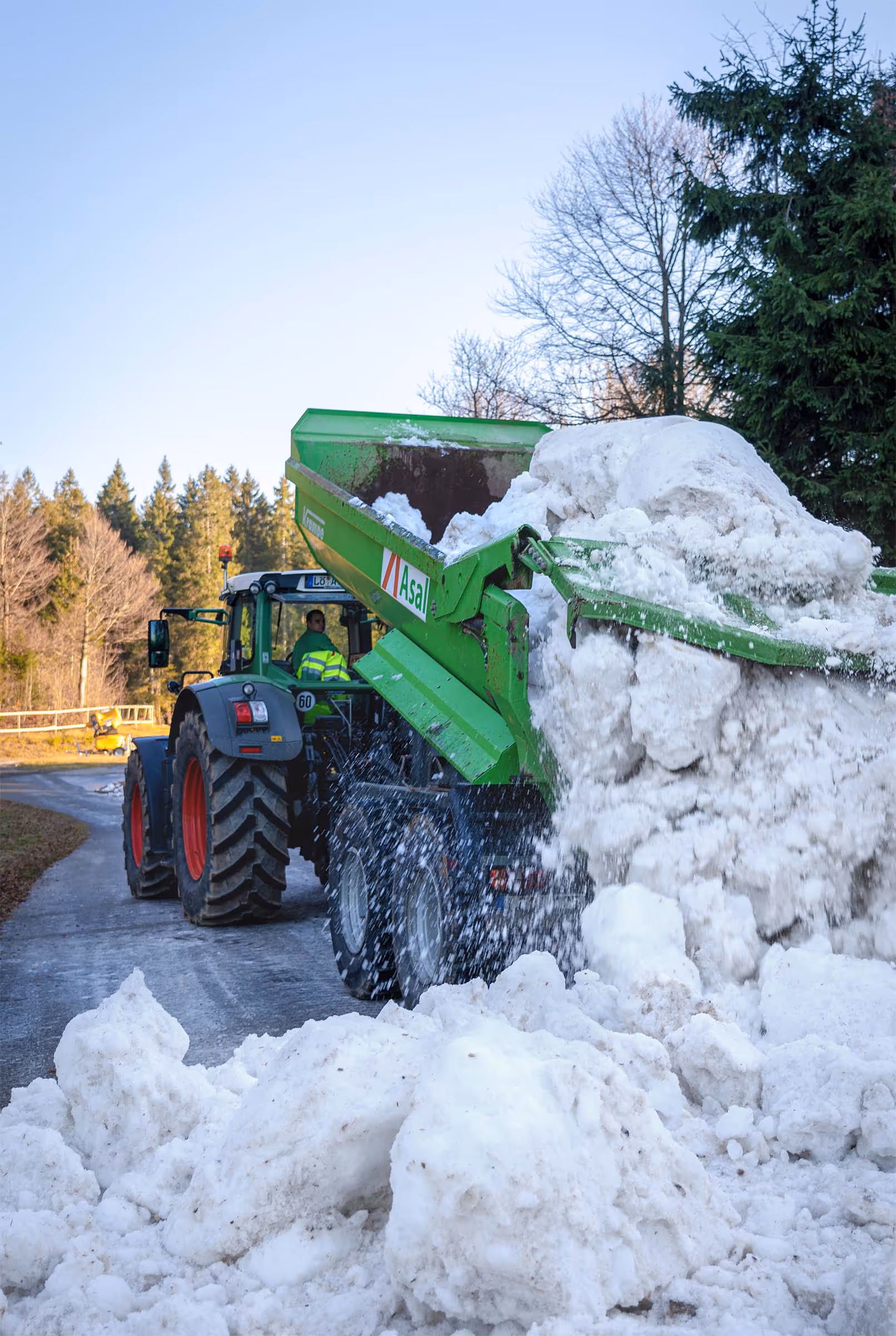 Radlader mit Schneeschild räumt in der Nacht bei starkem Schneefall eine Straße frei.