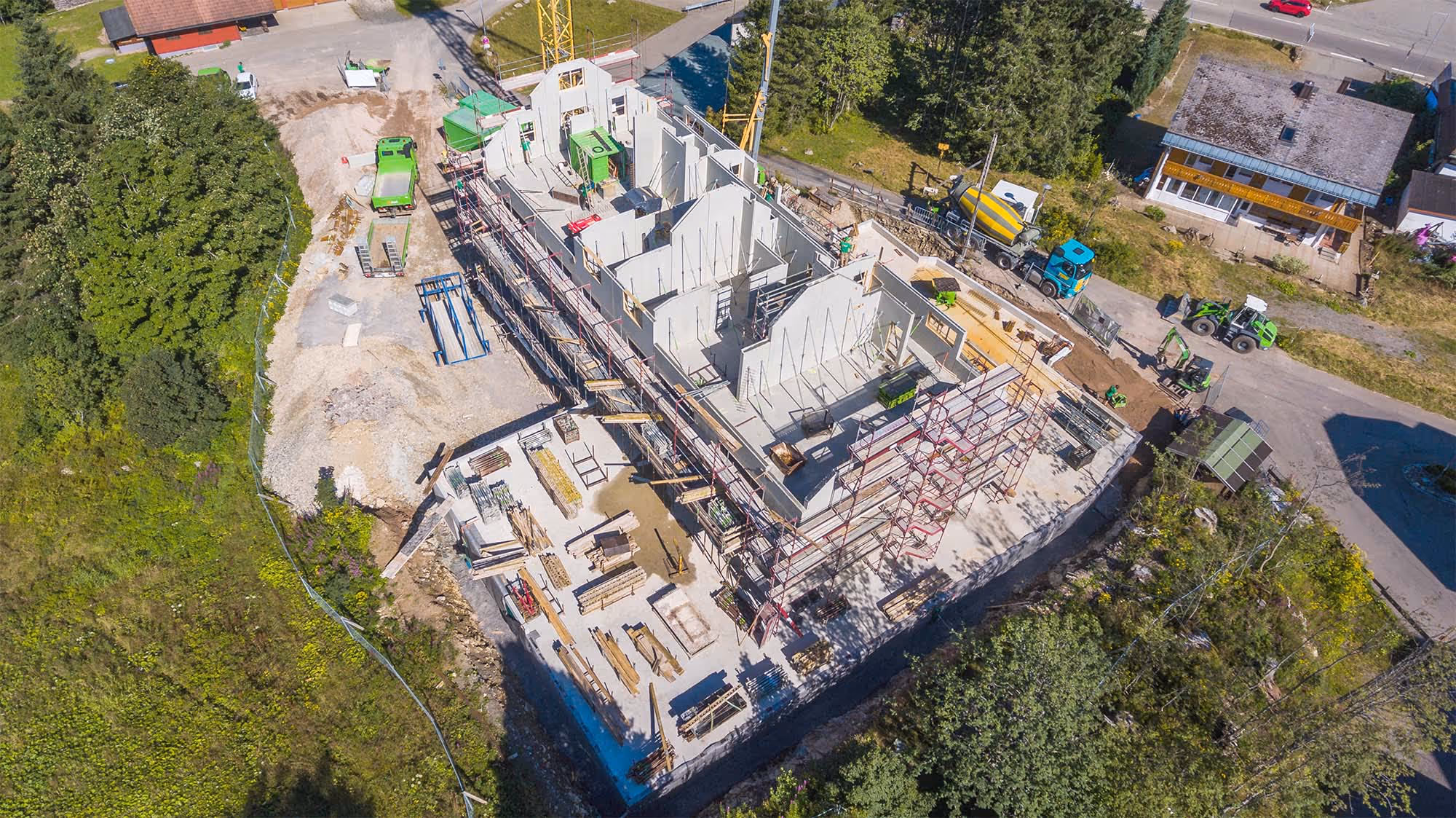 Luftaufnahme einer Baustelle mit bereits errichteten Betonwänden und eingerüstetem Rohbau.