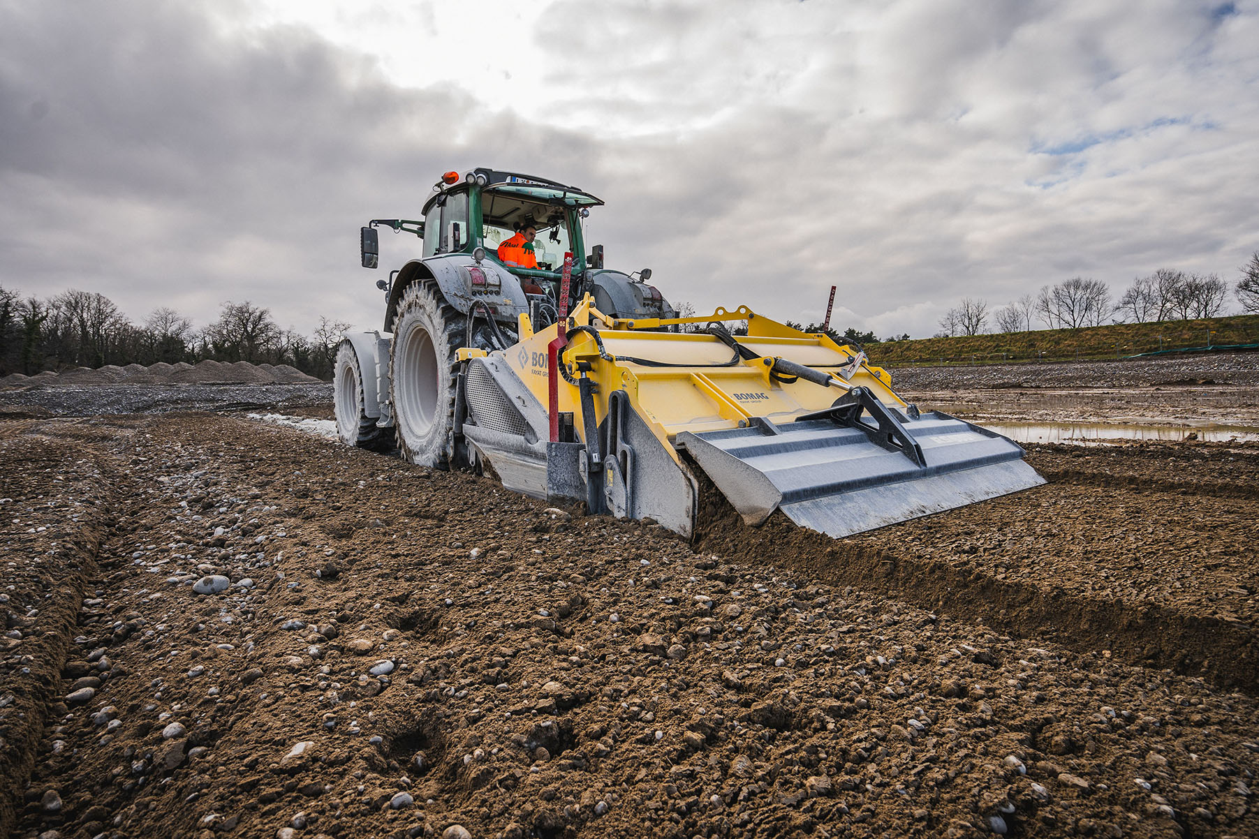 Traktor mit gelber Bodenfräse beim Stabilisieren von Bodenmaterial auf Baustelle.