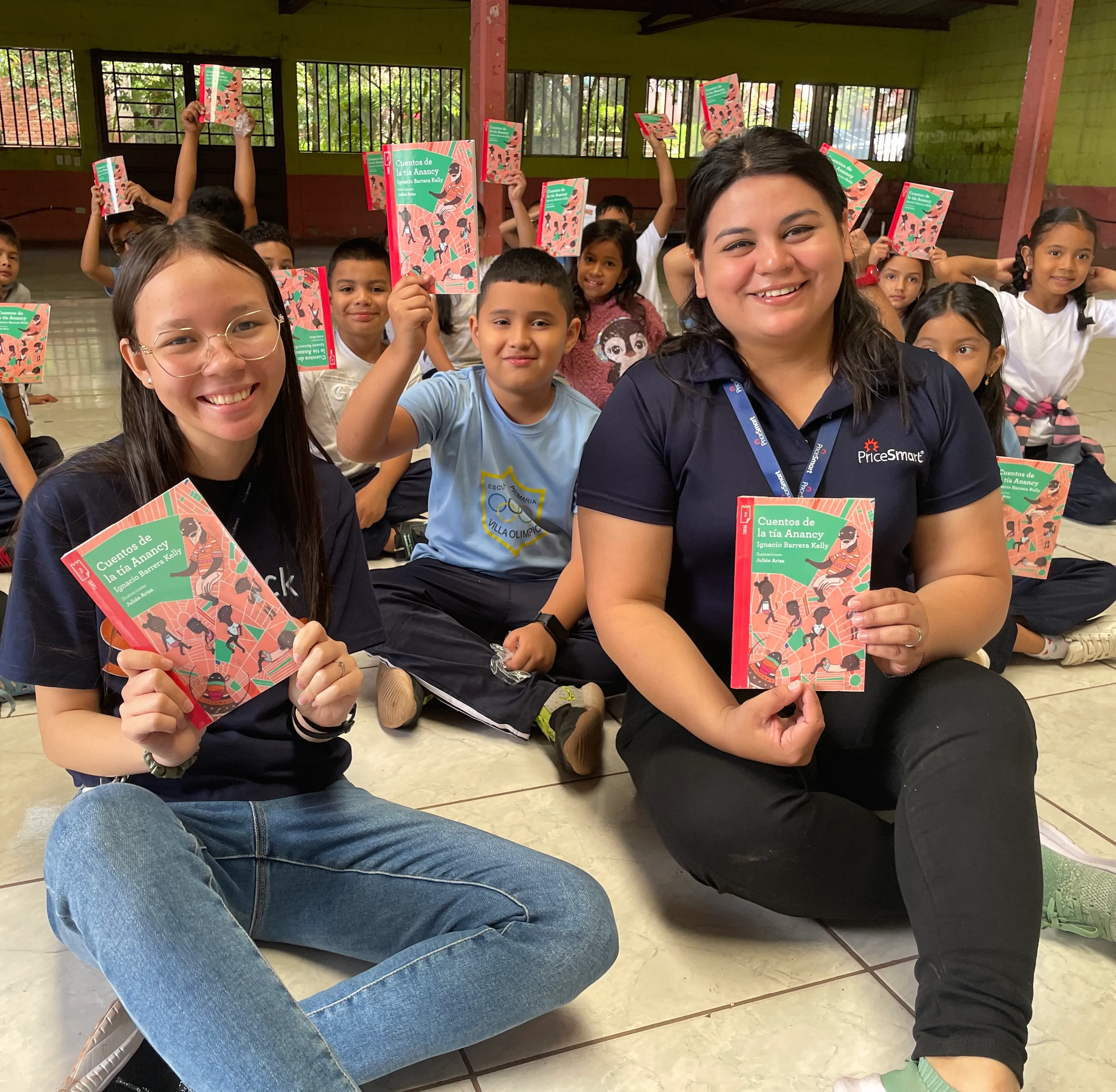 Two women and a group of children hold up copies of a book titled "Cuentos de la tía Anancy."