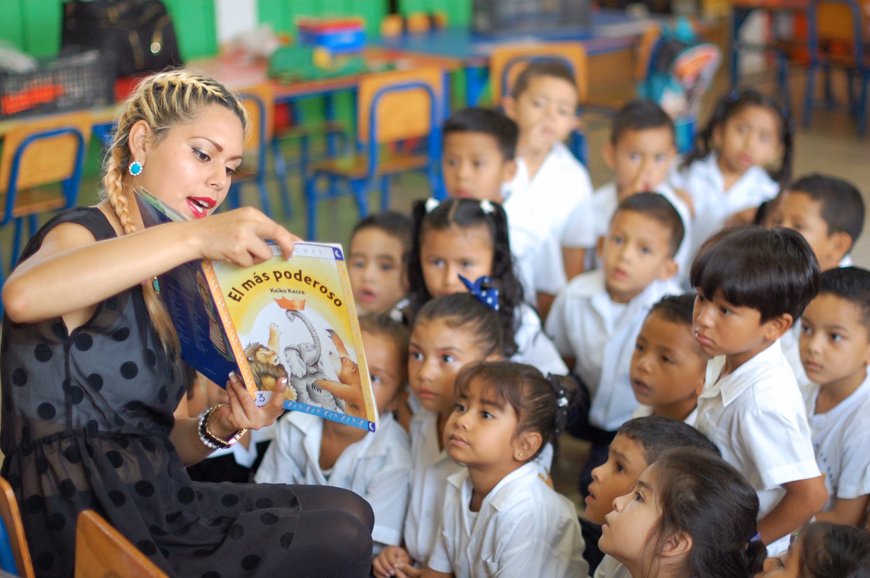 Teacher reading the book 'El más poderoso' to a group of attentive young students in a classroom.