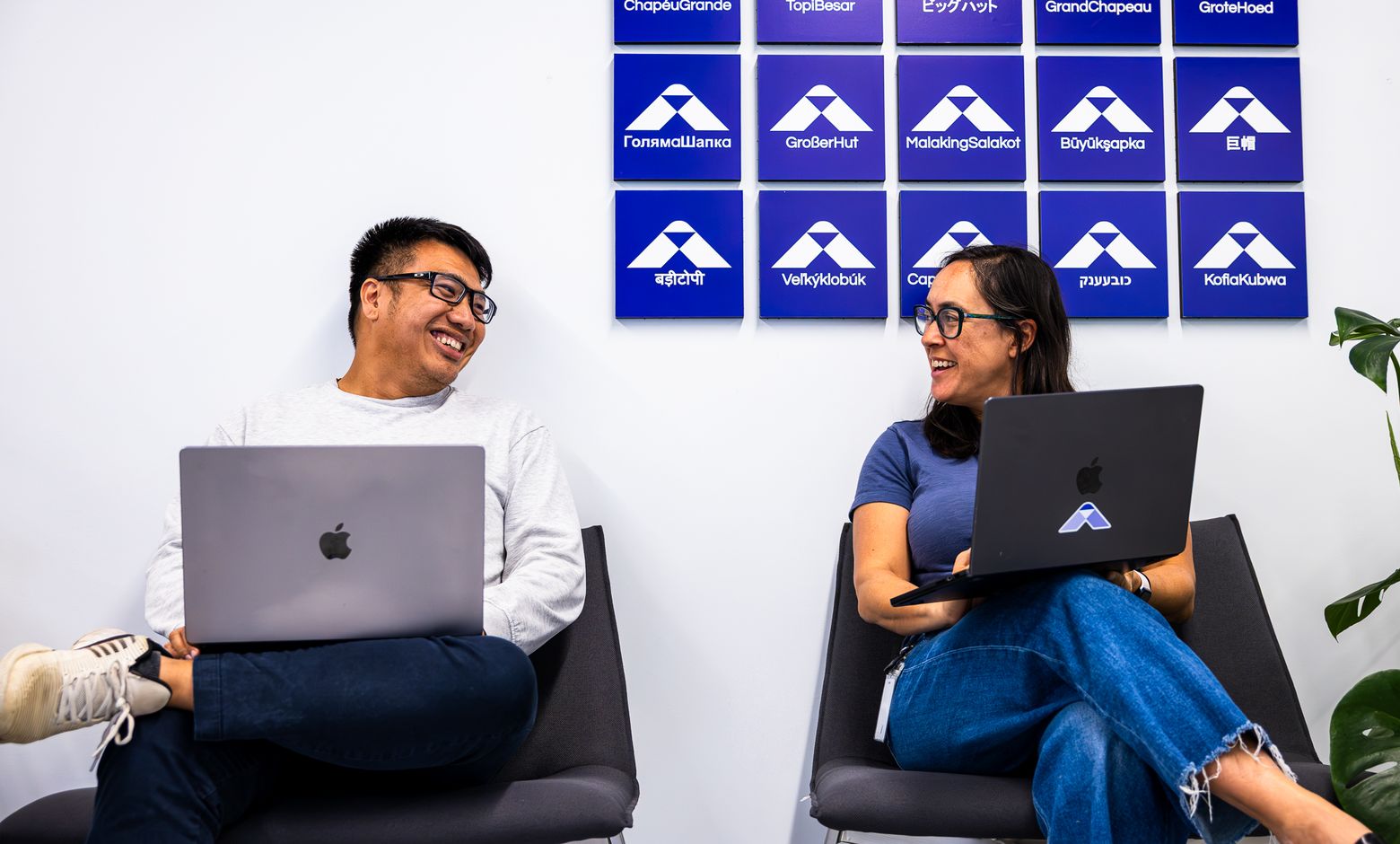 Two BigHat colleagues working on laptops beneath the BigHat logo wall