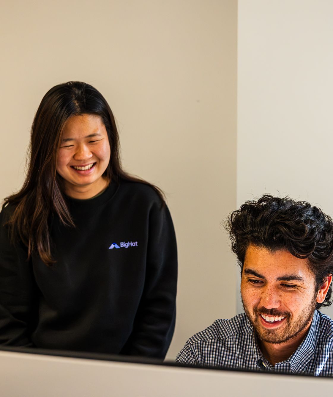 Two BigHat colleagues smiling while working together at a computer