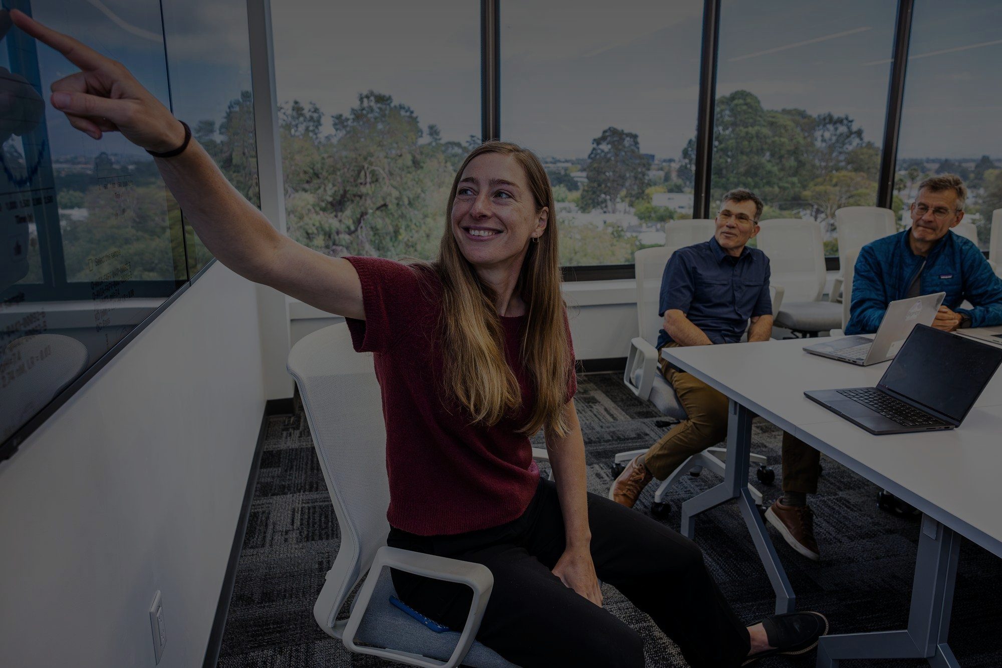 BigHat colleagues in a meeting room overlooking trees, one pointing to a screen