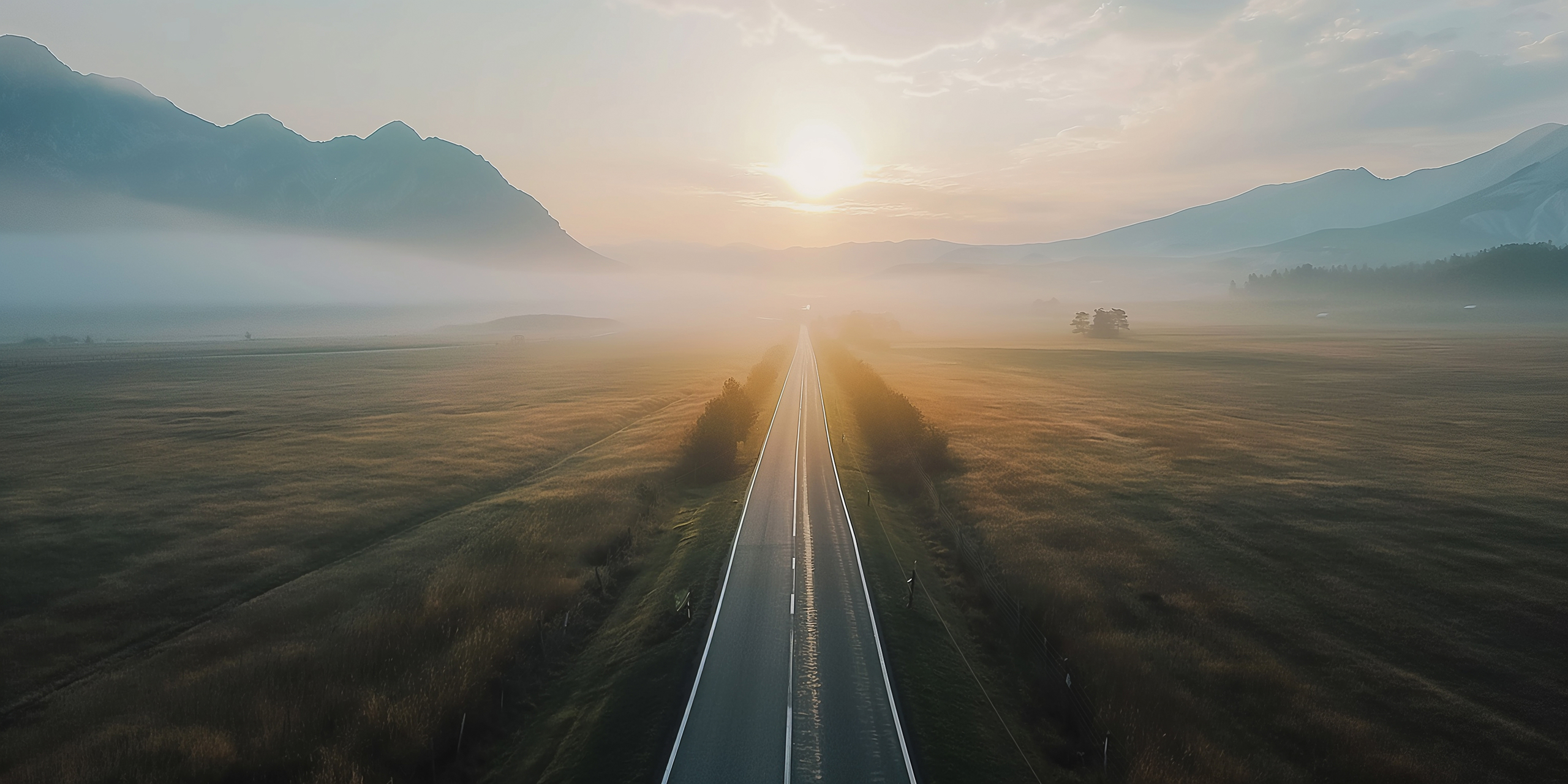 Road leading into sunny, mountainous, foggy landscape