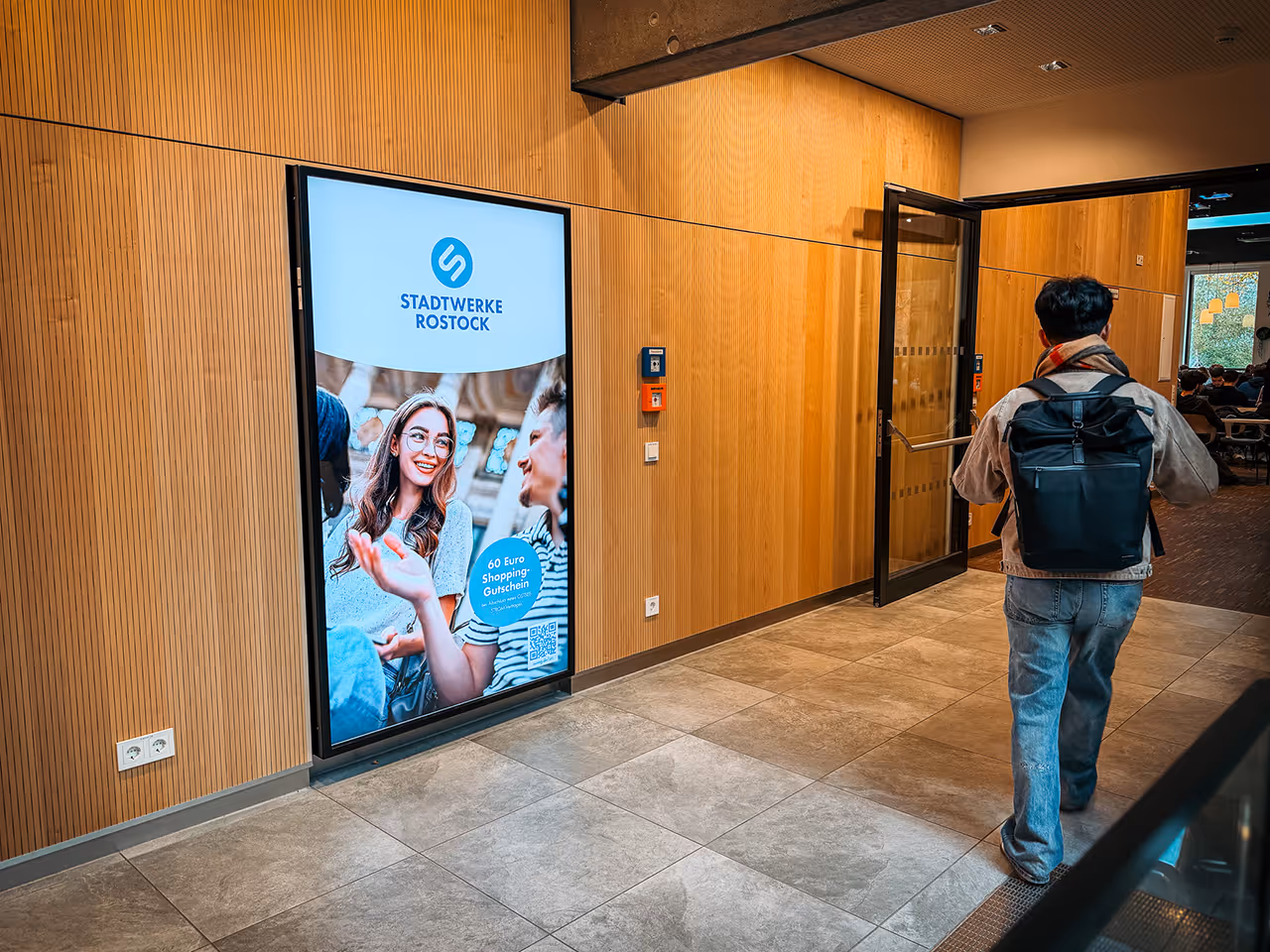Großes digitales XL Poster für Hochschulwerbung in der Mensa Ulme in Rostock. Ein Student geht daran vorbei. 