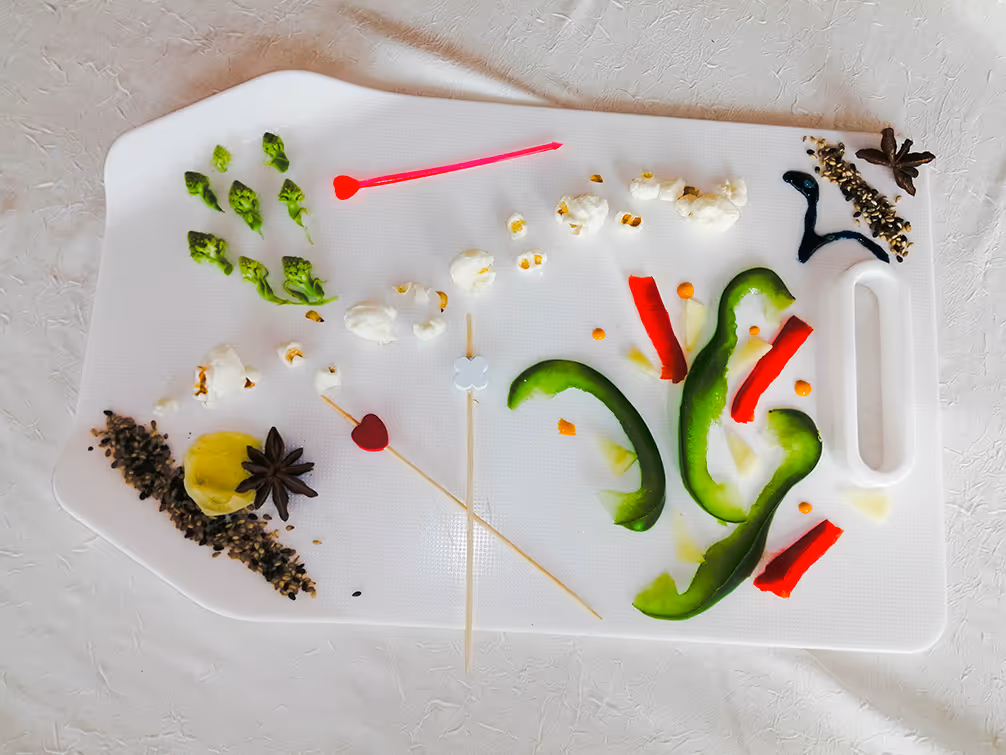 Planche blanche avec morceaux de poivrons verts et rouges, maïs soufflé, épices et pics à brochette.
