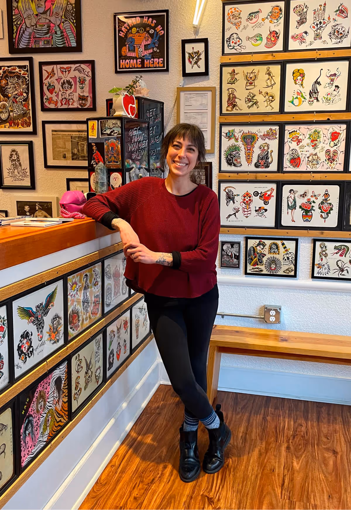 Brittany Quntero of Sweet Heart Tattoo, standing in front of a wall of flash art.