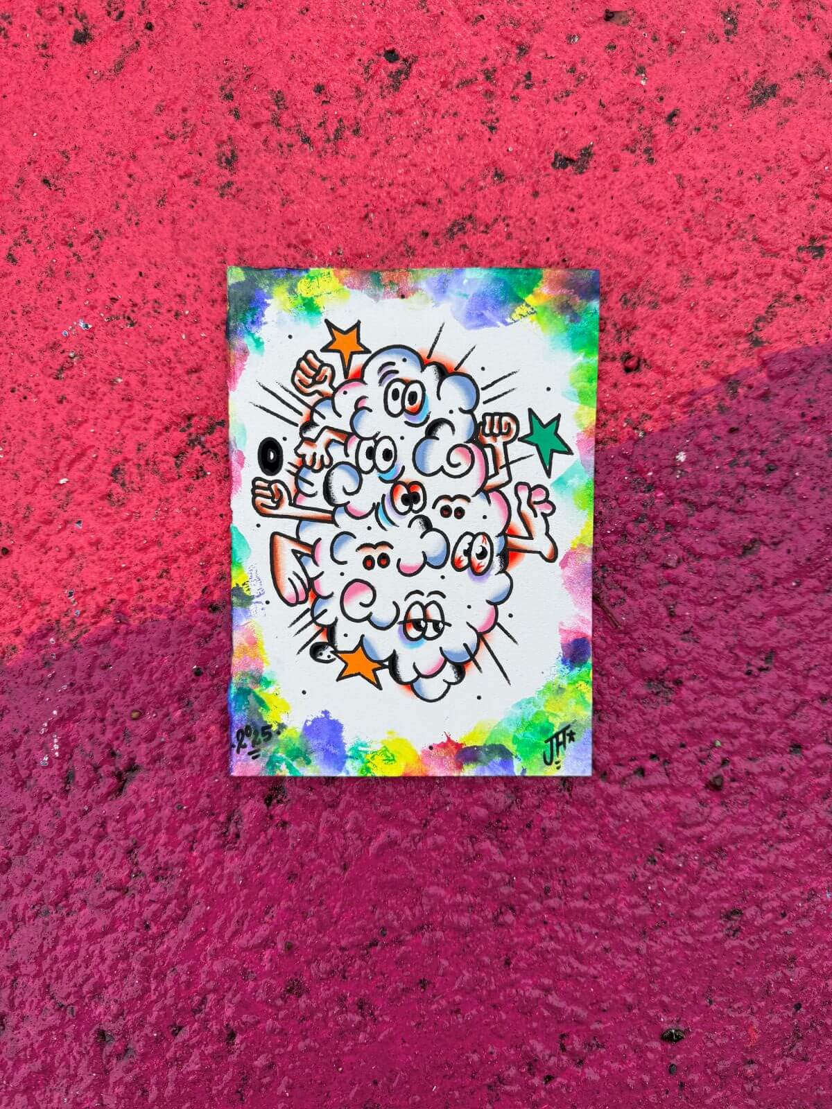 Colorful graffiti art of a cloud-like blob with multiple cartoon eyes, fists, arms, and orange and green stars on a white rectangular canvas, set against a red textured wall.