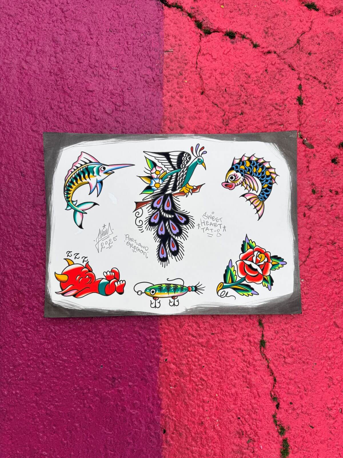 Tattoo flash sheet with colorful traditional designs including a marlin, peacock, fish, sleeping red devil, fishing lure, and rose on a white background with gray border.