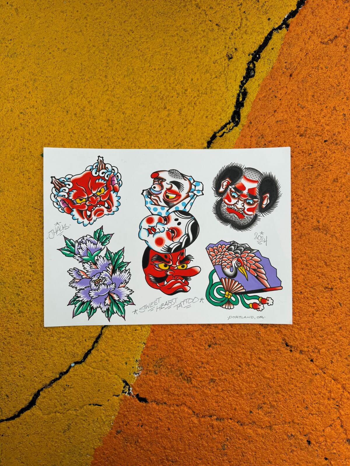 Sheet of colorful traditional-style tattoo flash designs from Sweet Heart Tattoo, including demon faces, a stack of Japanese masks, purple flowers, and a crane with a fan.