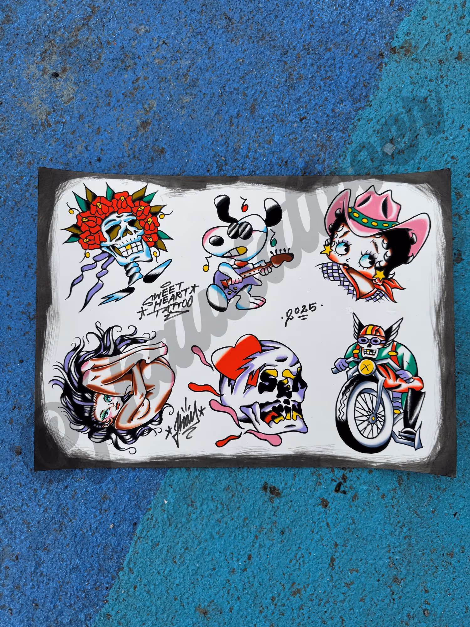 Tattoo flash sheet with colorful designs including a skull with rose crown, Snoopy playing guitar, Betty Boop cowgirl, curled-up woman, stylized skull with fire, and motorcyclist skeleton.