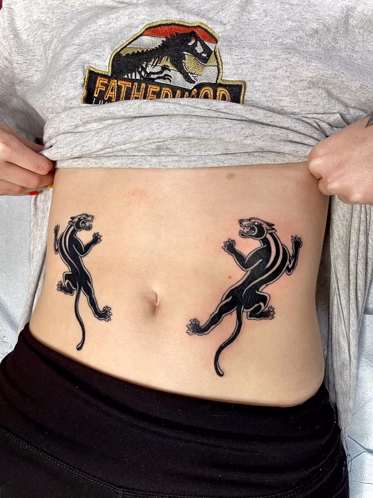 Two traditional-style black panther tattoos on the lower stomach on either side of the navel.