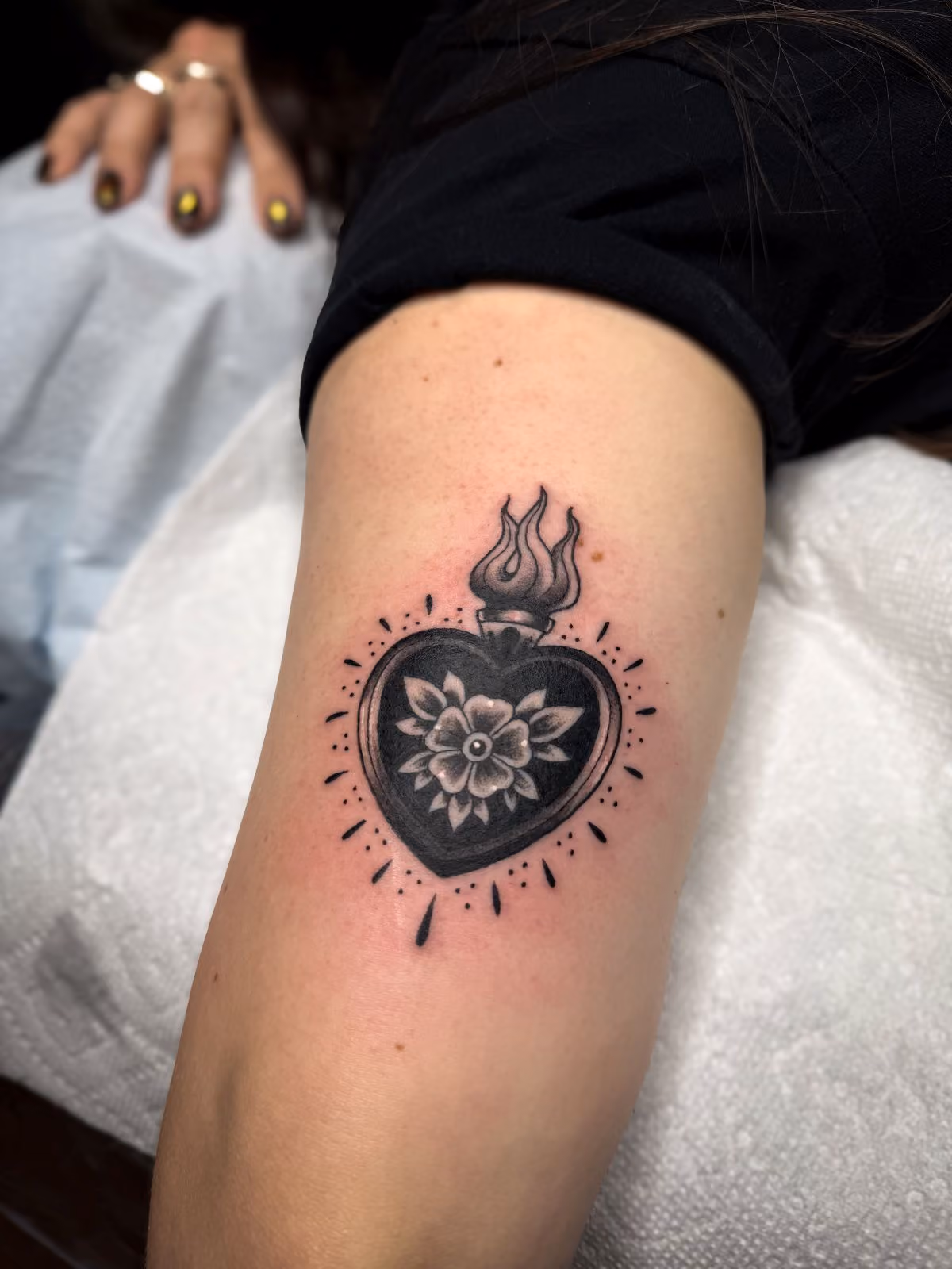 Black and grey sacred heart tattoo with a flower inside on a person's upper arm.