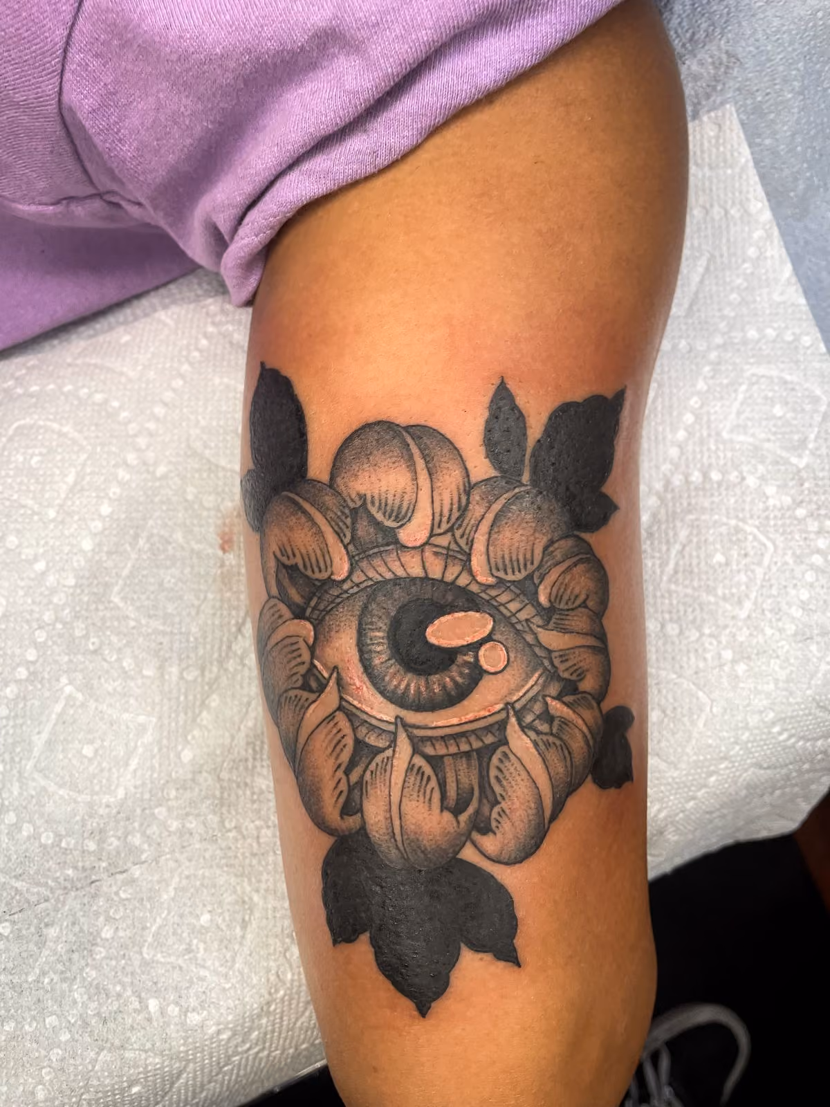 Black and gray tattoo of an eye surrounded by peony petals on a person's arm.