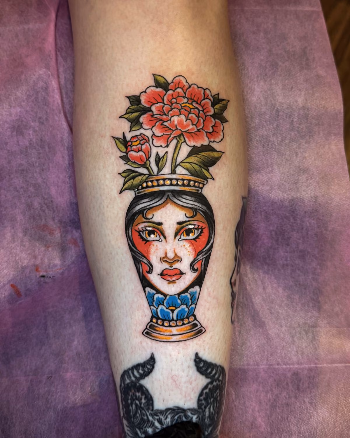 Colorful tattoo of a vase with a woman's face and flowers on a person's leg.