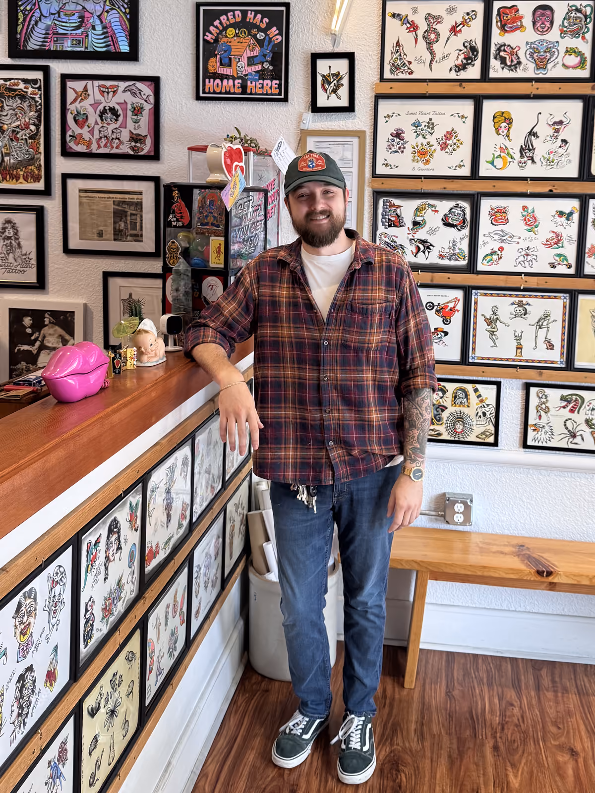 Bryce Bowerman of Sweet Heart Tattoo, leaning on counter, smiling.