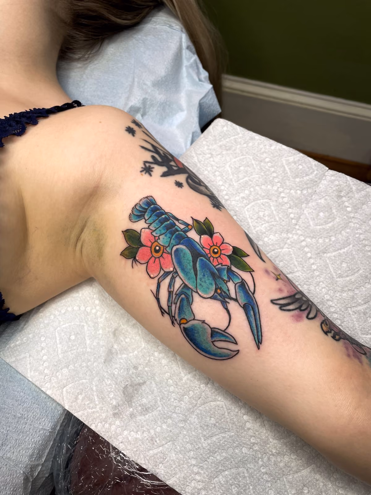 Blue crayfish tattoo with pink flowers on a person's upper arm.