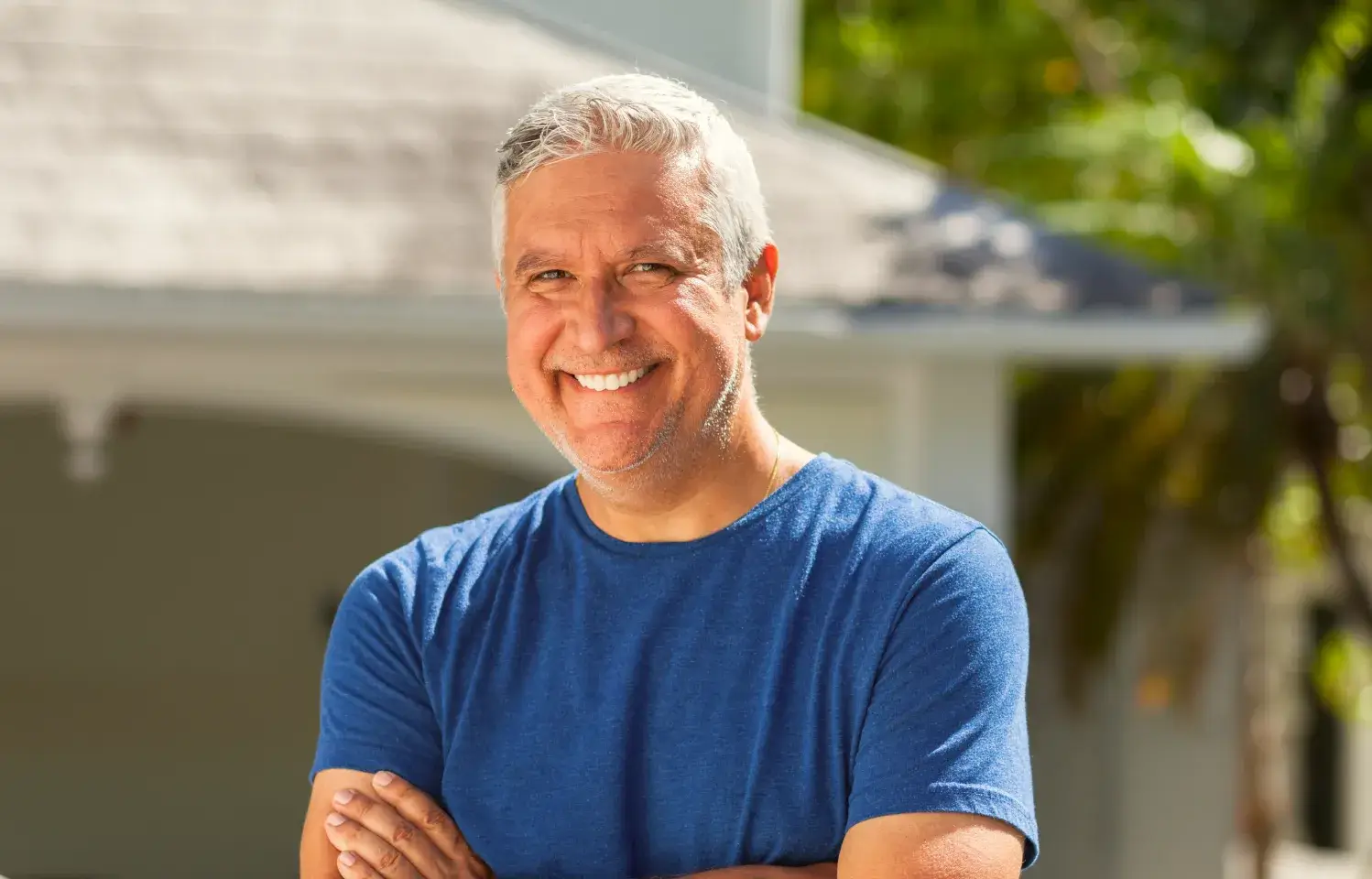 a man with his arms crossed standing in front of a house