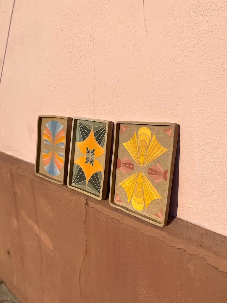 Colorful, hand painted ceramic trays lined up in a row against a pink wall. 