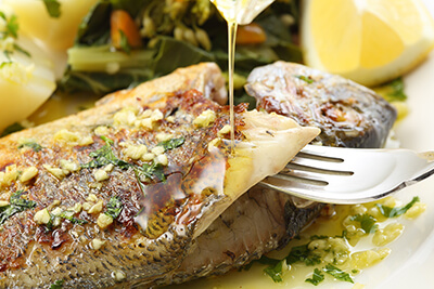 Primer plano de un lomo de pescado fresco asado a la espalda con majado de ajo y perejil, regado con un hilo de aceite de oliva