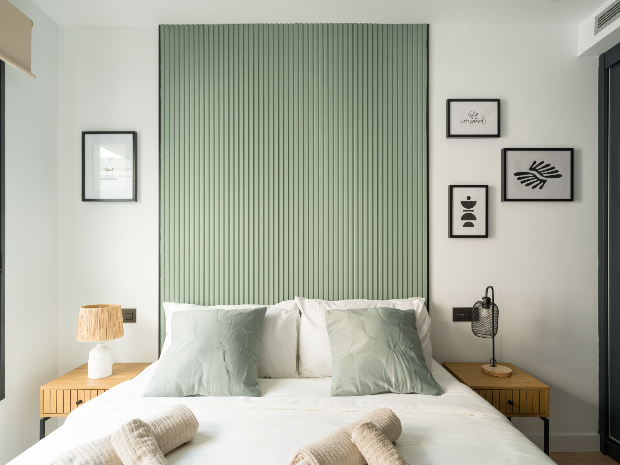 Dormitorio principal moderno de un apartamento turístico con un cabecero alistonado en verde sabio, mesitas de madera y decoración nórdica