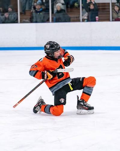 Young orange jersey hockey player celebrates on one knee during a game