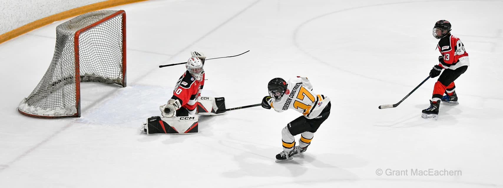 Real youth hockey game with a shooter taking a shot near a red-jersey goaltender