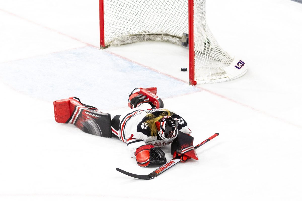 Youth hockey goaltender lies face down on the ice with the puck behind the goal line after a difficult moment