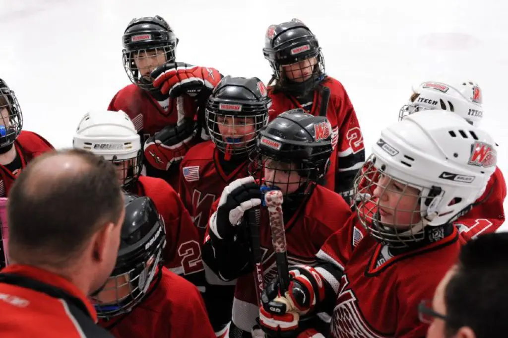 Hockey coach viewed from behind speaking with a group of young players in red uniforms; illustrative photograph, not Kevin Grant.