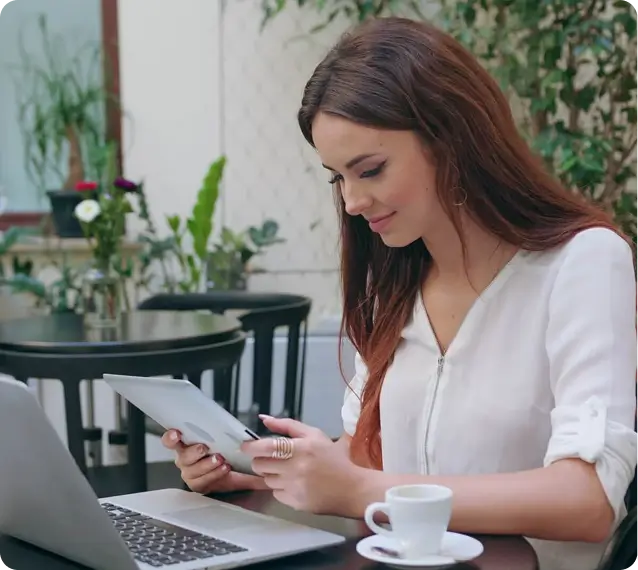lady in a corporate  setting using her tablet. there is a coffee mug and a laptop widely opened