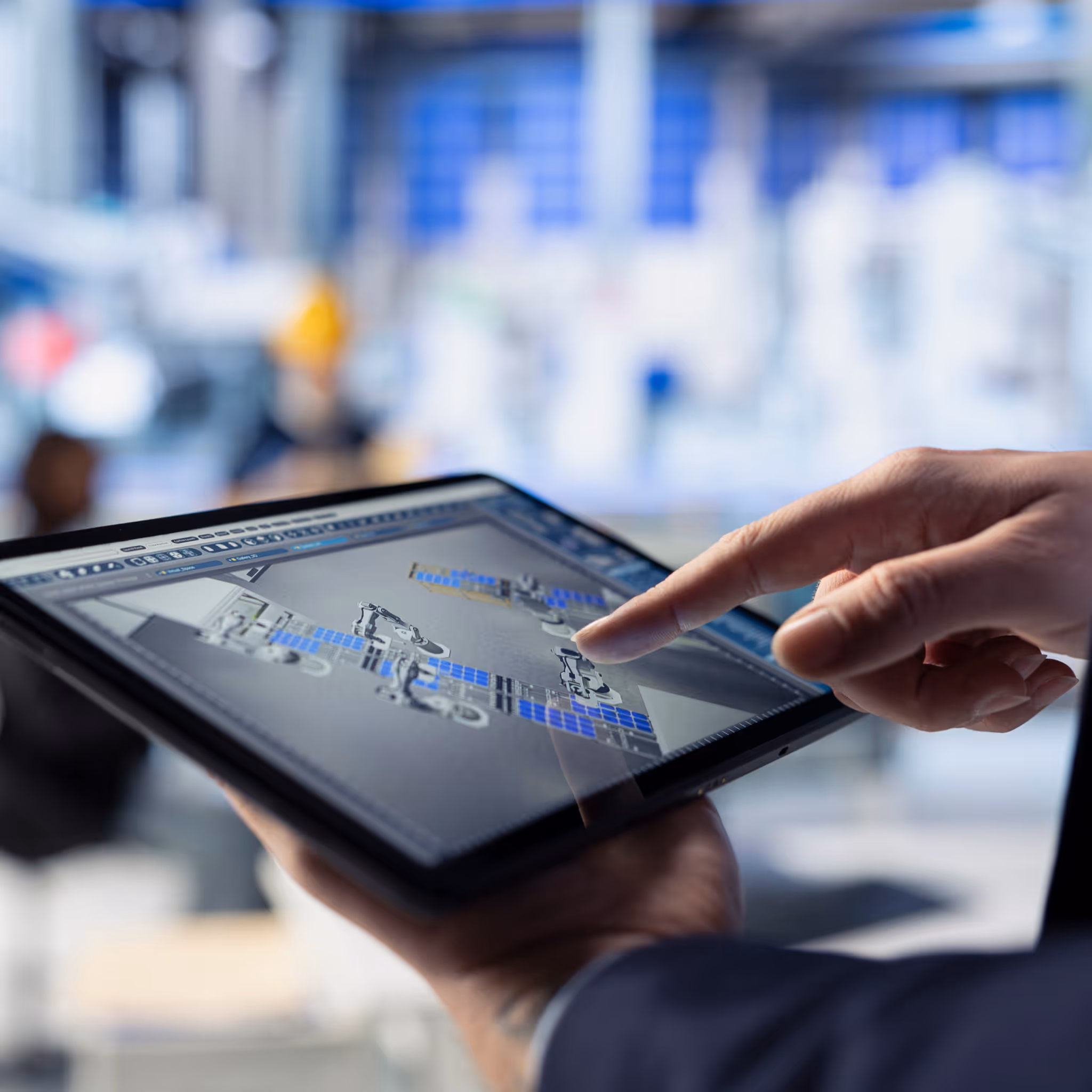 Close-up of a person in a dark suit interacting with a tablet displaying a digital design of robotic arms and industrial automation equipment. The blurred background suggests a factory or workshop setting. The image reflects ITR’s expertise in smart automation and industrial technology solutions for modern manufacturing environments.