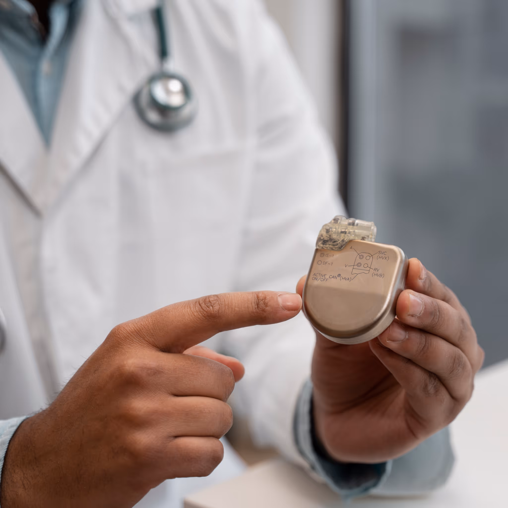Close-up of a person in a white lab coat with a stethoscope holding and pointing at a metallic pacemaker device labeled with anatomical terms such as “SVC” and “RA.” The image highlights ITR’s expertise in advanced MedTech solutions and medical device innovation, set in a professional healthcare environment.
