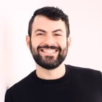 Smiling man with dark hair and beard wearing a black shirt against a light background.