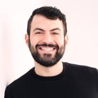 Smiling man with dark hair and beard wearing a black shirt against a light background.
