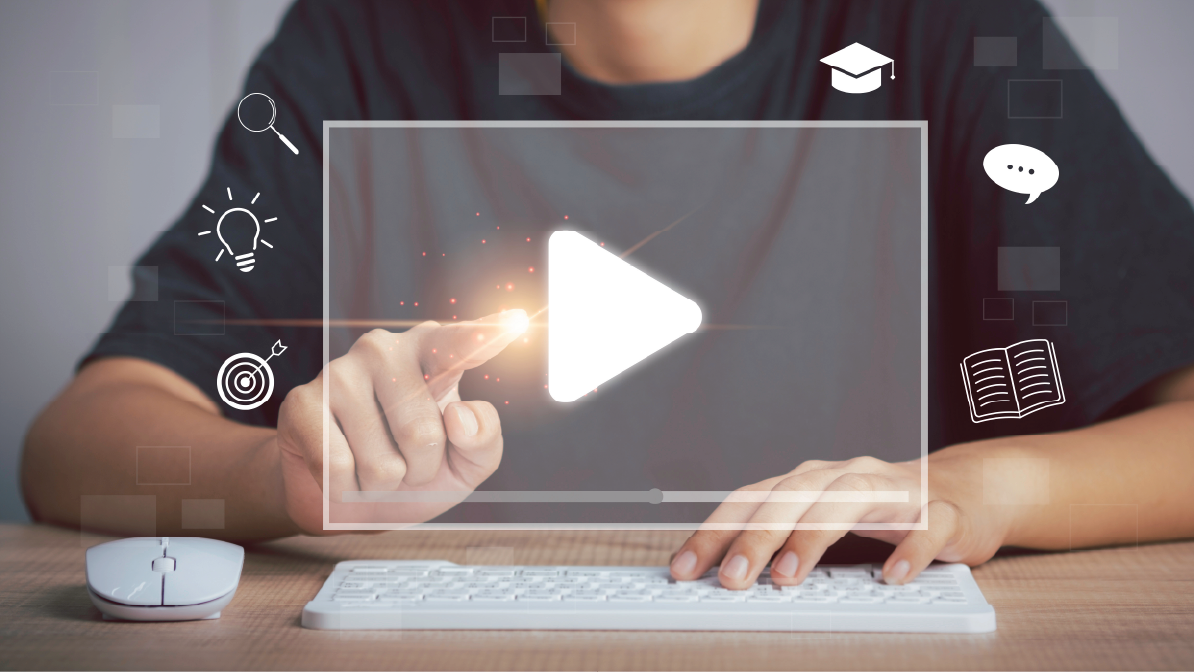 A photograph of a man in a dark grey t-shirt, sat at a computer with a keyboard in front of him. On the screen is a giant play button, and the man is pressing it.