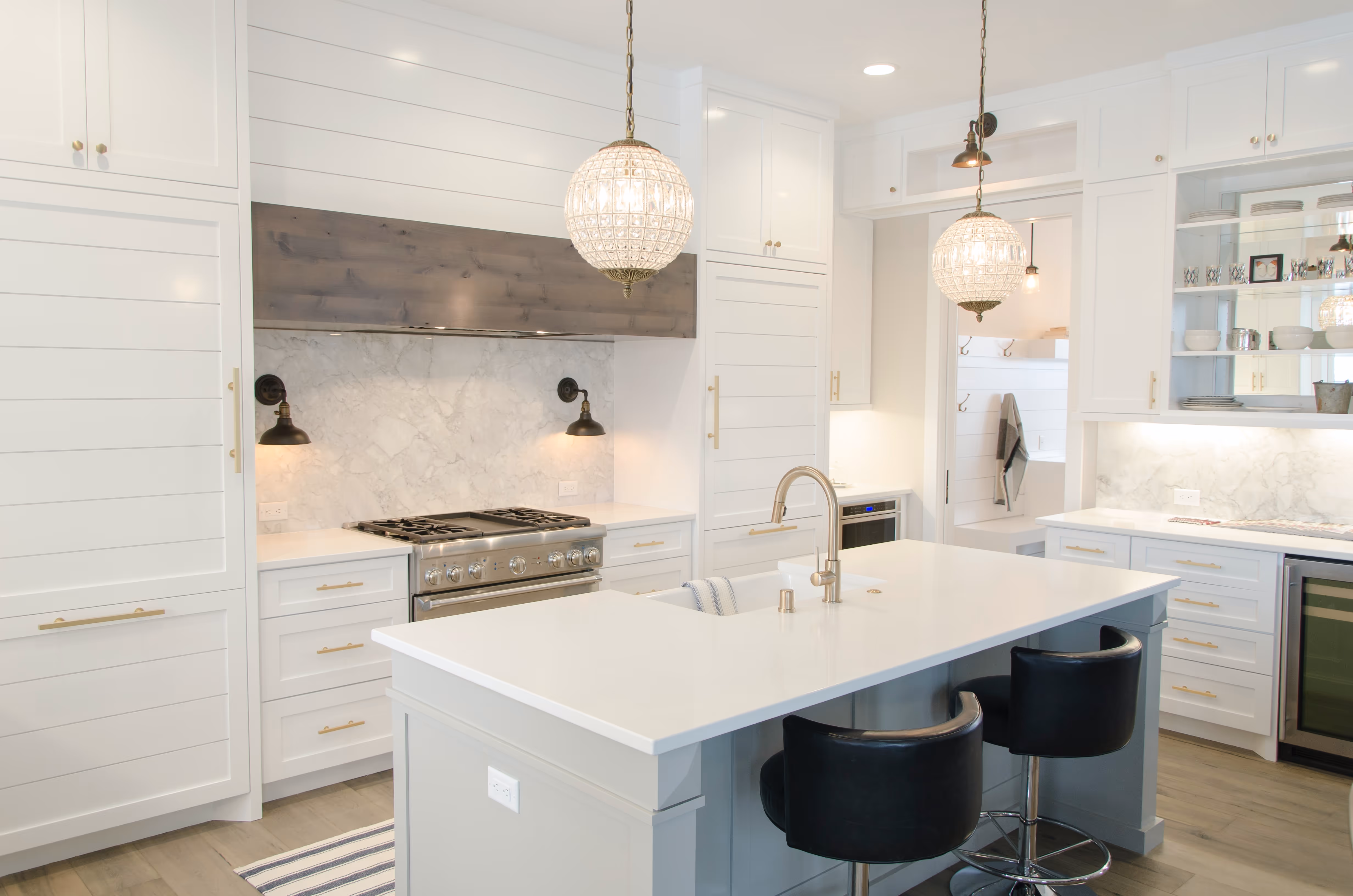 Modern kitchen with white cabinetry, marble backsplash, a large island with sink, two black bar stools, and pendant lights.