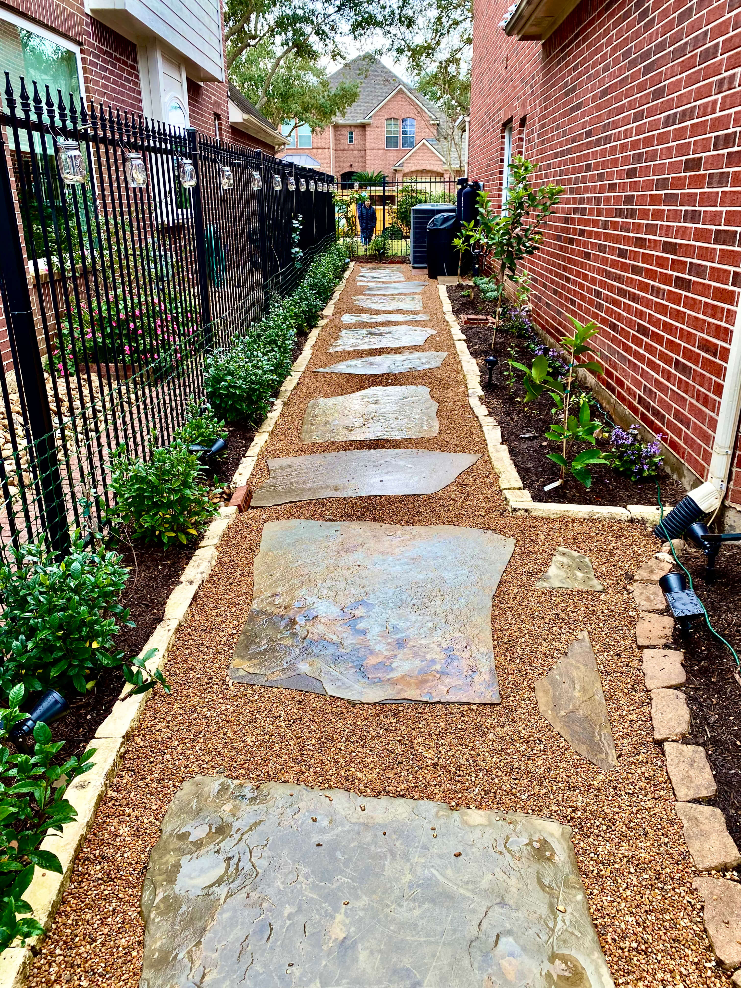 Finished side yard landscape design with stone walkway, gravel path, edging, shrubs, and planting beds.