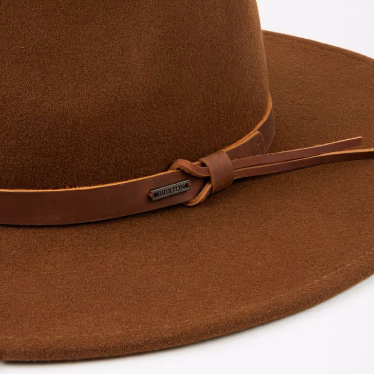 Close-up of a brown felt fedora hat with a leather band and a metal Brixton logo tag.