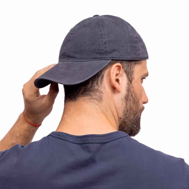 Man wearing a backward dark gray baseball cap and navy blue shirt, viewed from behind, adjusting the cap with his left hand.